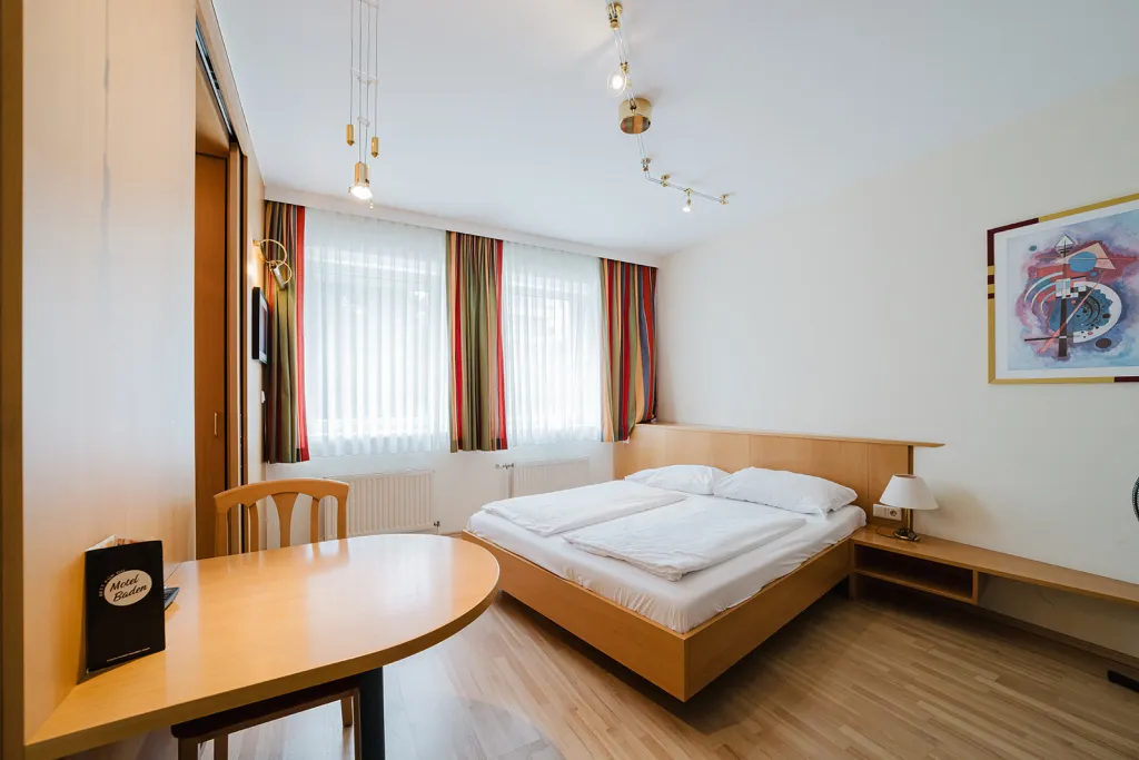 Helles Zimmer mit Doppelbett, Holzmöbeln und Tisch im Motel Baden