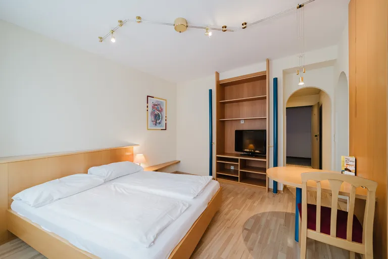 Room with double bed, desk, and wall unit with TV at Motel Baden