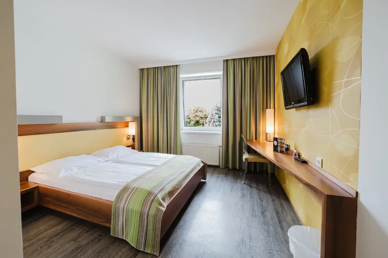 Double bed in front of a yellow accent wall with flat-screen TV at Motel Baden