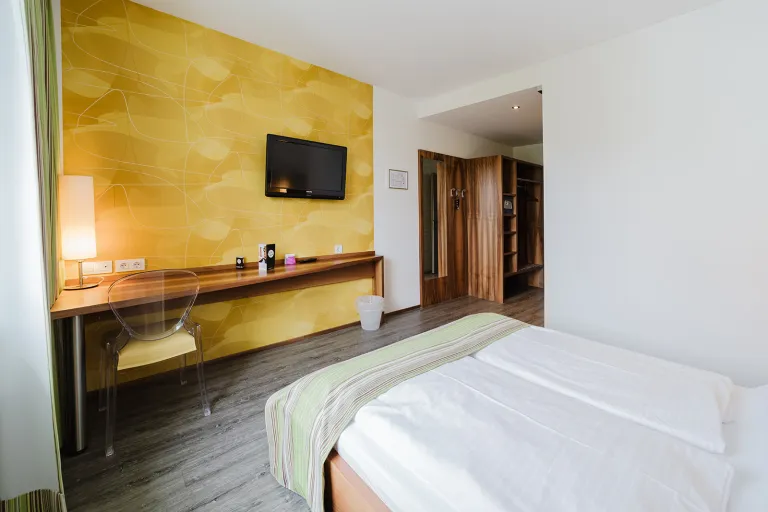 Double room with yellow accent wall, flat-screen TV, desk, and double bed at Motel Baden