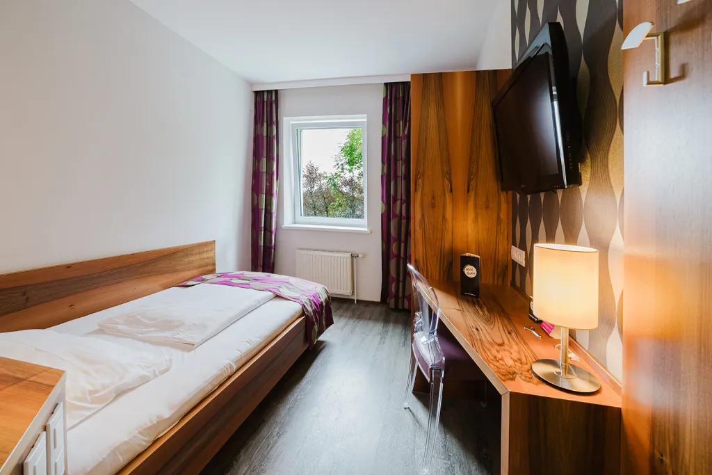 Einzelzimmer mit Bett, Holzwand mit Flat-TV und Schreibtisch im Motel Baden