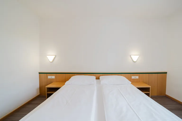 Modern double room with two beds pushed together and wall lights at Motel Baden
