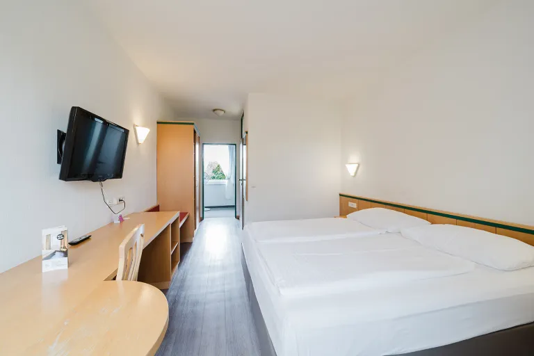 Modern double room with wall-mounted TV, desk and double bed at Motel Baden