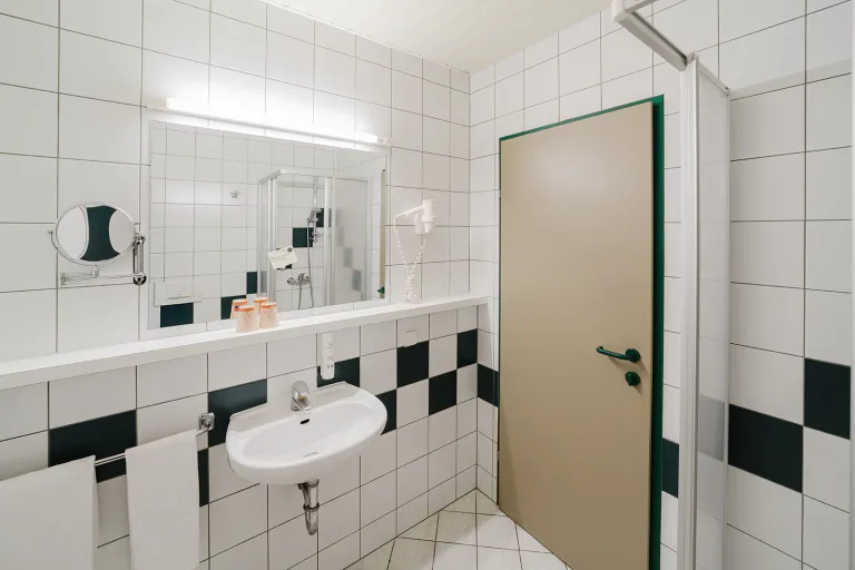 Vanity with mirror in the green-and-white tiled bathroom at Motel Baden